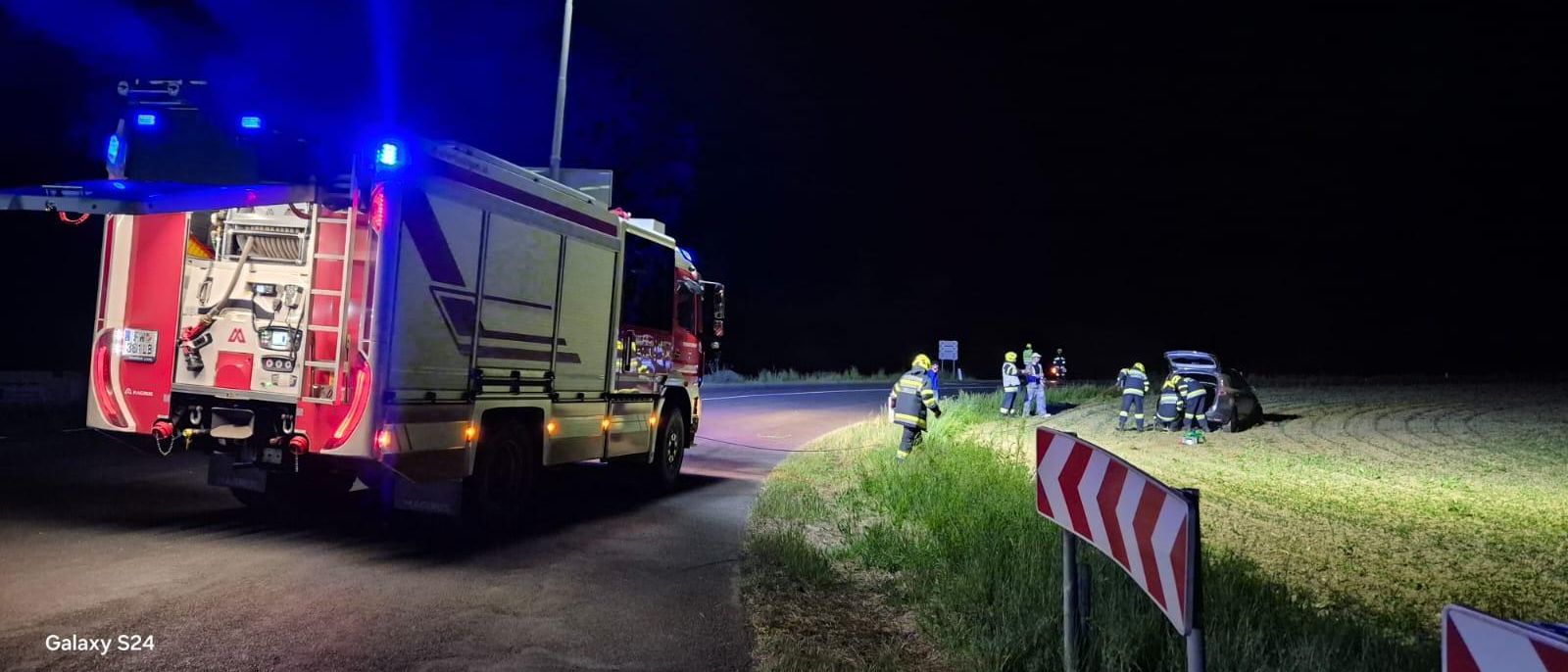 Ein Feuerwehrwagen ist nachts am Straßenrand geparkt, mit versammeltem Notfallpersonal.