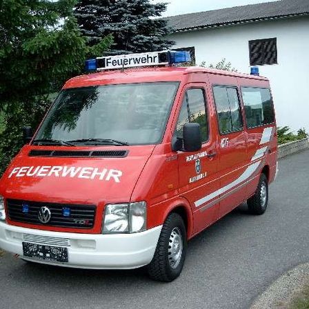 Ein roter Feuerwehrwagen mit weißen Markierungen ist auf einer Einfahrt vor einem weißen Haus mit Balkon geparkt.