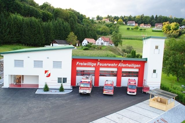 Luftaufnahme einer Feuerwehrstation mit roten und weißen Fahrzeugen davor. Die Station heißt Freiwillige Feuerwehr Allerheiligen.