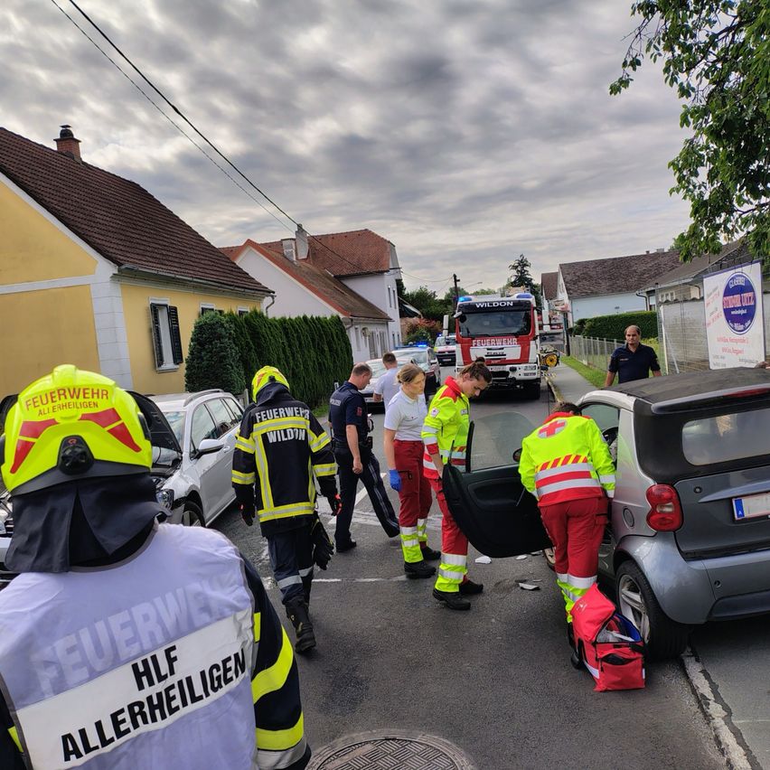 Rettungskräfte, einschließlich Feuerwehrleute und Sanitäter, kümmern sich um einen Autounfall auf einer Straße. Das Auto ist offen, und die Helfer untersuchen das Fahrzeug.