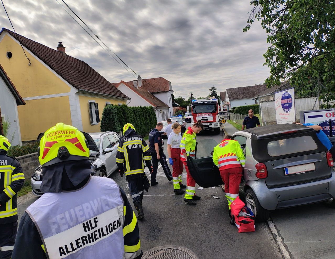 Rettungskräfte, einschließlich Feuerwehrleute und Sanitäter, kümmern sich um einen Autounfall auf einer Straße. Das Auto ist offen, und die Helfer untersuchen das Fahrzeug.