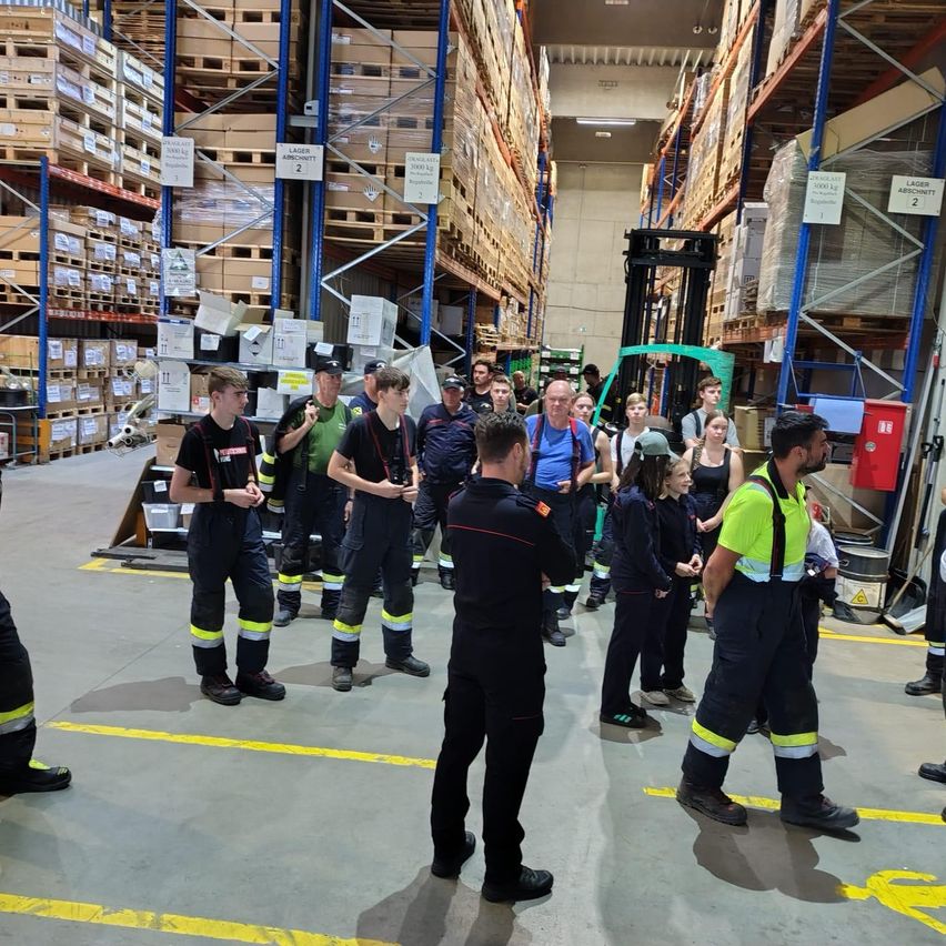 Eine Gruppe von Menschen in Uniformen steht in einem Lager. Eine Person spricht mit einer anderen Person vor ihnen.