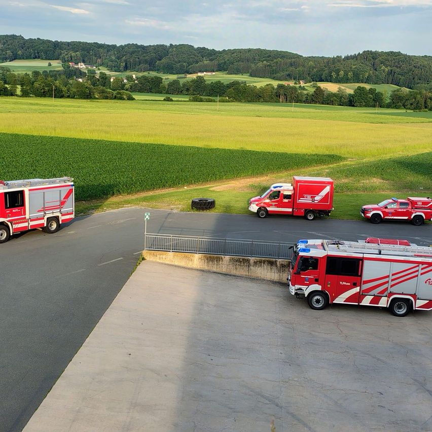 Auf einem Hügel sind vier Feuerwehrfahrzeuge in einem ländlichen Gebiet mit einem großen grünen Feld und fernen Hügeln unter klarem Himmel geparkt.