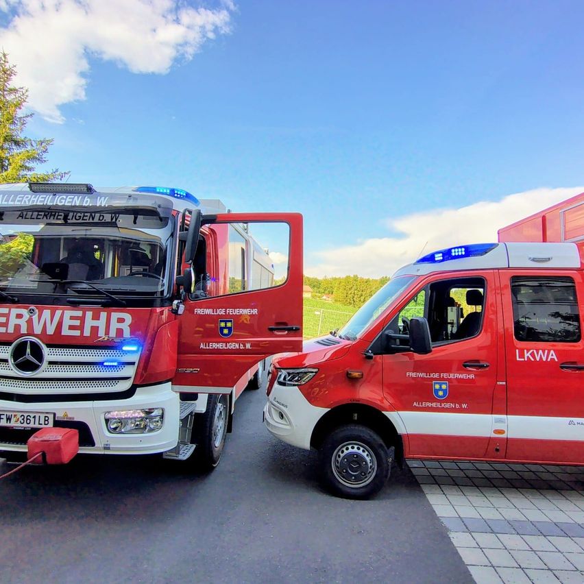 Zwei rote Einsatzfahrzeuge sind geparkt, eines mit offenen Türen. Das Fahrzeug auf der linken Seite ist ein Mercedes-Benz Feuerwehrauto, und das auf der rechten Seite ist ein Polizeifahrzeug.