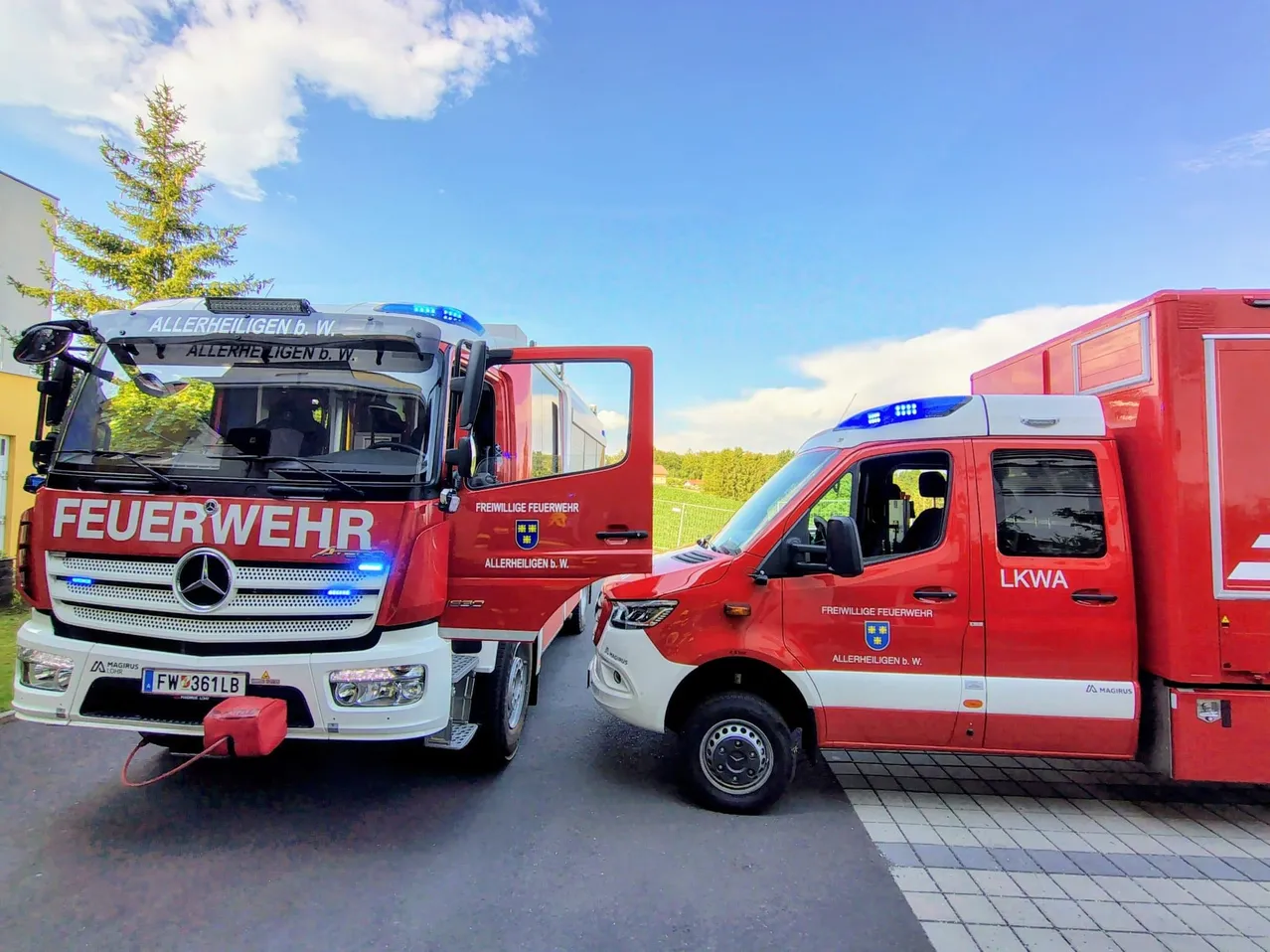 Zwei rote Einsatzfahrzeuge sind geparkt, eines mit offenen Türen. Das Fahrzeug auf der linken Seite ist ein Mercedes-Benz Feuerwehrauto, und das auf der rechten Seite ist ein Polizeifahrzeug.