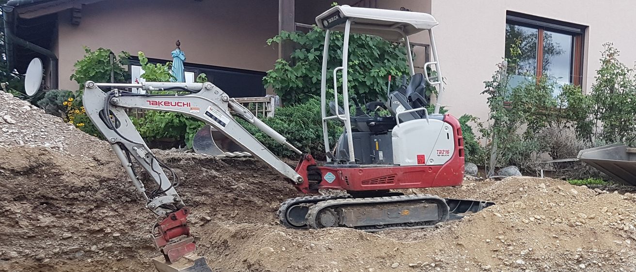 Ein roter und weißer Bagger steht auf einem Haufen Erde. Dahinter steht ein Haus mit Pflanzen und einem Fenster.