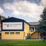 Ein großes gelbes und blaues Gebäude mit einem Schild, das 'Bildungs- und Kulturzentrum' steht in einem Grasbereich mit Bäumen und einem Spielplatz im Vordergrund.
