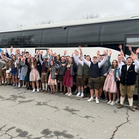Eine Gruppe von Menschen in traditioneller deutscher Kleidung posiert für ein Foto vor einem Bus.