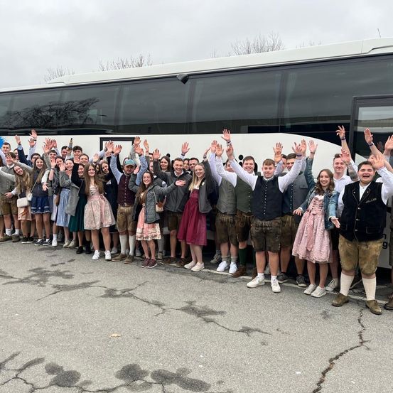 Eine Gruppe von Menschen in traditioneller deutscher Kleidung posiert für ein Foto vor einem Bus.