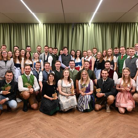 Eine Gruppe von Menschen in traditioneller Kleidung posiert für ein Foto in einem Raum mit grünen Vorhängen.