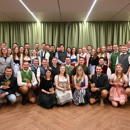 Eine Gruppe von Menschen in traditioneller Kleidung posiert für ein Foto in einem Raum mit grünen Vorhängen.