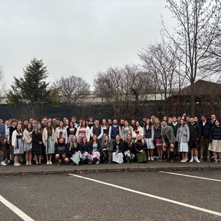 Eine Gruppe von Menschen in traditioneller deutscher Kleidung posiert für ein Foto auf einem Parkplatz.
