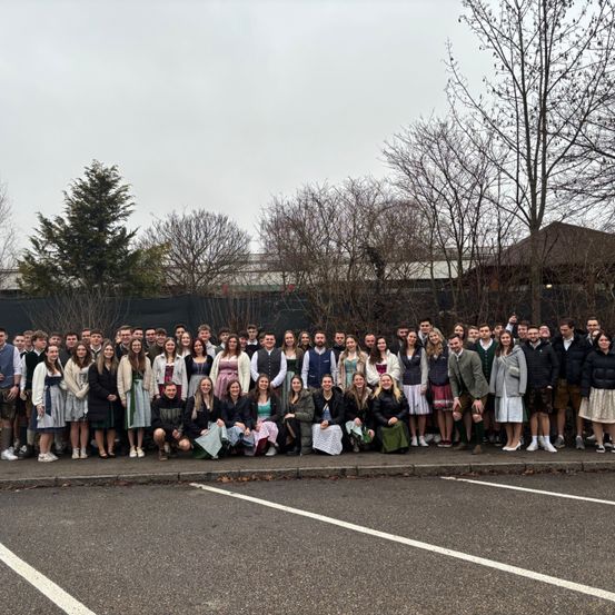 Eine Gruppe von Menschen in traditioneller deutscher Kleidung posiert für ein Foto auf einem Parkplatz.