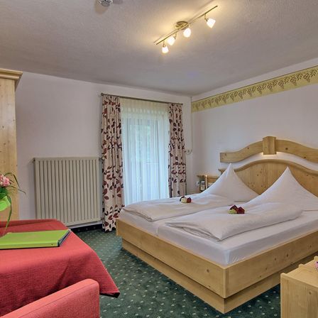 Ein gemütliches Hotelzimmer mit einem Doppelbett, Holzmöbeln, einem weißen Heizkörper und einem kleinen Tisch mit Blumenvase.