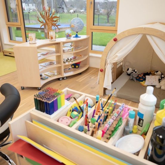 Ein Spielzimmer mit einem Zelt und einem Holzschreibtisch voller bunter Bastelutensilien. Hinter dem Schreibtisch steht ein Globus und ein Bücherregal.