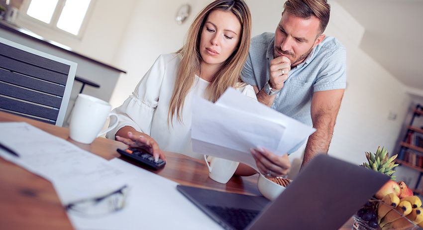 Ein Paar schaut sich Rechnungen an und benutzt einen Taschenrechner, während es in einer Küche an einem Schreibtisch sitzt.