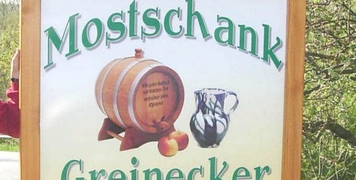 Ein Schild für Mostschank Greinerecker zeigt einen Fass, eine Kanne und Äpfel. Es enthält Öffnungszeiten und eine Nachricht, dass es an Feiertagen geschlossen ist.