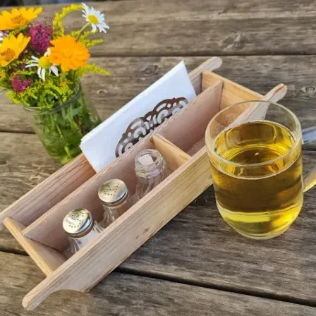 Ein Holztablett mit Salz- und Pfefferstreuer, einer Vase mit Blumen und einer Tasse Tee steht auf einem Holztisch.