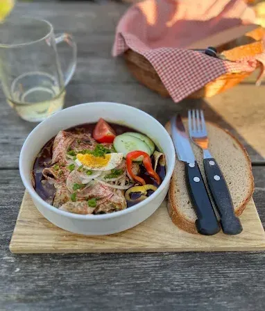 Eine Schüssel mit Fleischeintopf und Gemüse, einem Messer und einer Gabel auf einem Holzschneidebrett.