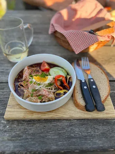 Eine Schüssel mit Fleischeintopf und Gemüse, einem Messer und einer Gabel auf einem Holzschneidebrett.