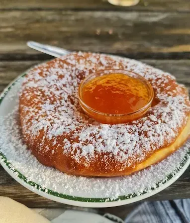 Ein runder Gebäck mit Puderzucker und einem kleinen Glas Marmelade darauf, auf einem Holztisch.