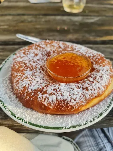 Ein runder Gebäck mit Puderzucker und einem kleinen Glas Marmelade darauf, auf einem Holztisch.
