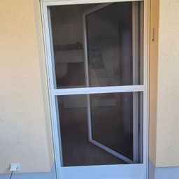 Eine offene weiße Schiebetür mit Glasscheibe und Moskitonetz, an einer beigefarbenen Wand montiert, gewährt einen Blick ins Innere.