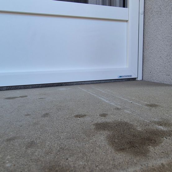 Ein Nahaufnahme einer weißen Schiebetür mit einem grauen Betonboden, der einige Schmutzflecken und Kratzer auf dem Boden zeigt.