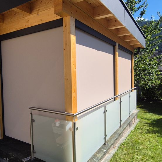 Das Äußere eines Hauses mit einem hölzernen Dach und weißen Rollos. Das Haus hat eine Glasbrüstung und einen Rasenbereich.