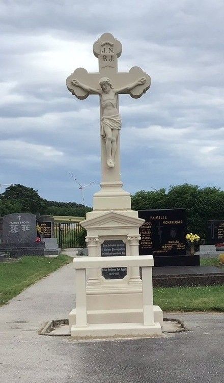 Ein großes Kreuzmonument auf einem Friedhof mit Jesus Christus darauf, umgeben von Grabsteinen und einer Rasenfläche.