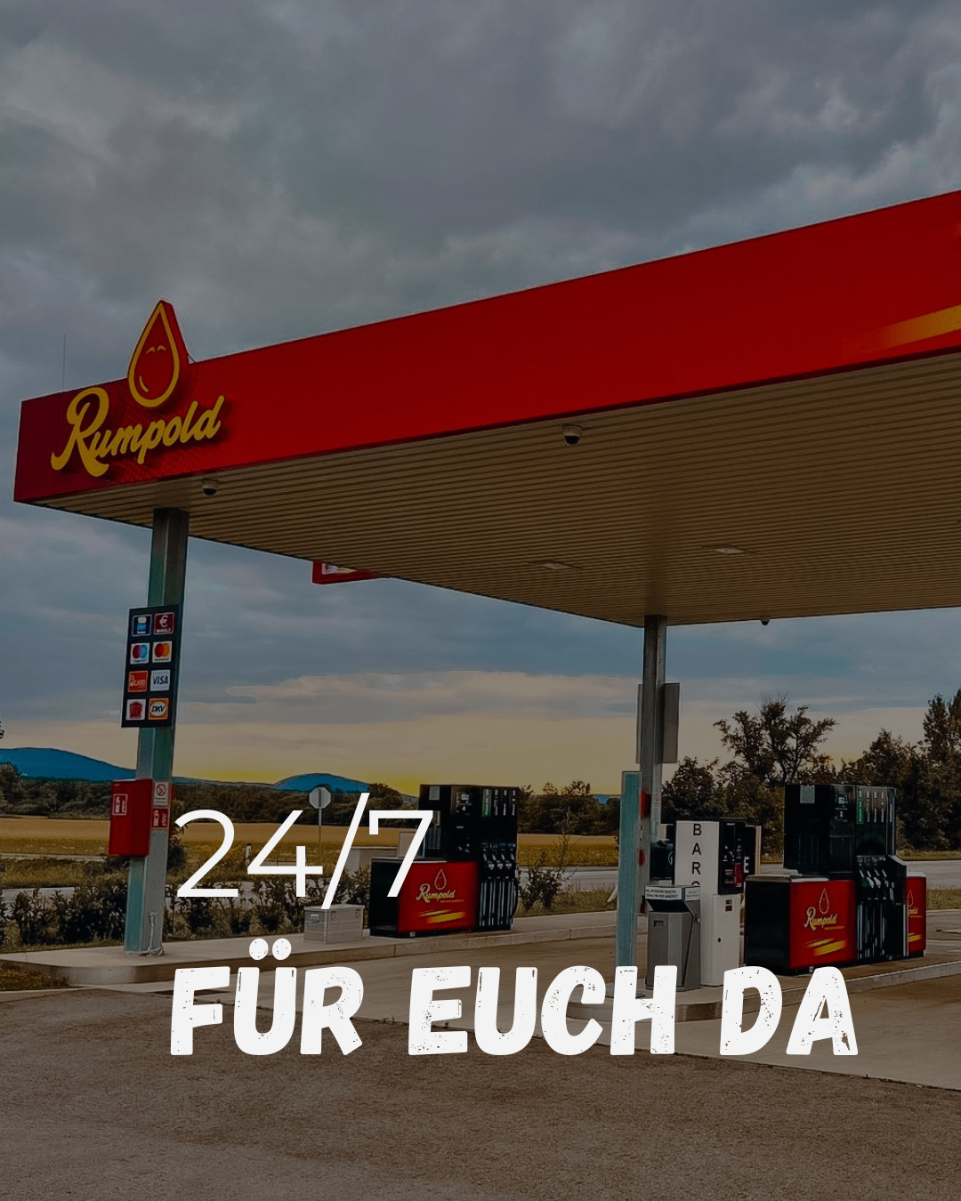 A gas station with a red canopy and the brand name Rumpold. The station is open 24/7. Payment options are displayed on the sign.