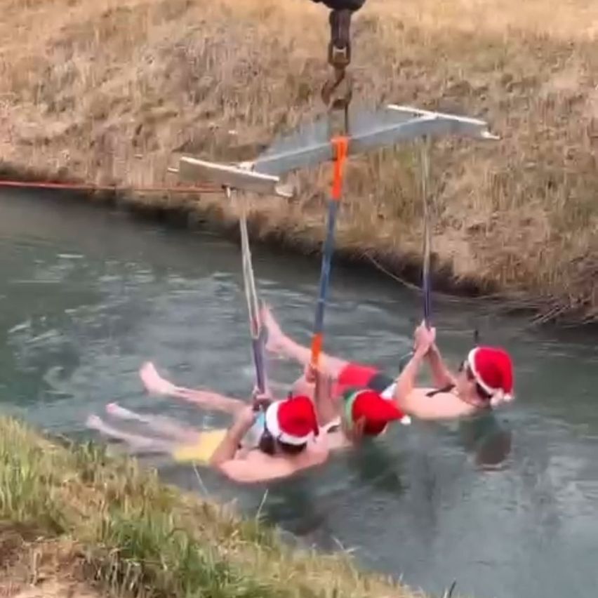 Vier Personen mit Weihnachtsmützen hängen im Wasser, möglicherweise für ein festliches Ereignis, wobei eine Person eine Metallstruktur festhält.