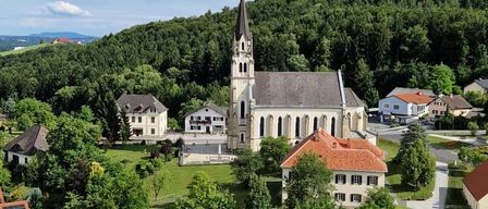 Luftaufnahme eines ruhigen Dorfes mit einer großen Kirche, umgeben von Häusern und üppiger Grünfläche.