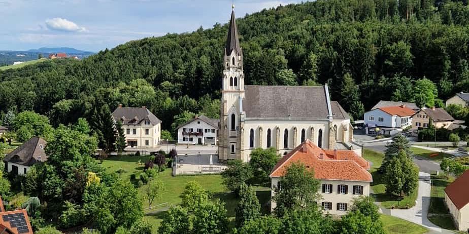 Luftaufnahme eines ruhigen Dorfes mit einer großen Kirche, umgeben von Häusern und üppiger Grünfläche.
