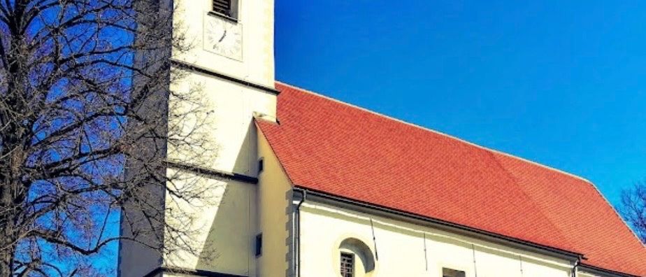 Eine weiße Kirche mit rotem Dach und Turm steht auf einem Hügel unter blauem Himmel.