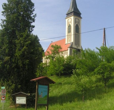 Eine Kirche mit rotem Dach und Turm steht auf einem grasigen Hügel unter einem blauen Himmel.