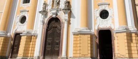 Ein gelbes und weißes Barockgebäude mit verzierten Statuen und Rundbogenfenstern.