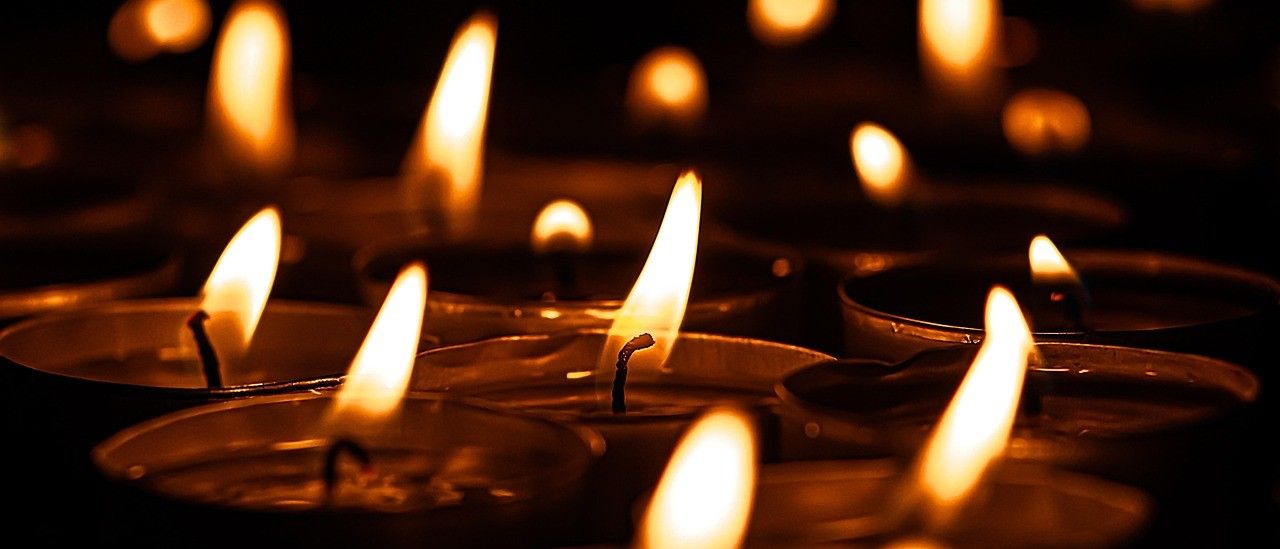 Eine Sammlung von Kerzen mit gelben Flammen in Metallhaltern, auf einem dunklen Hintergrund platziert.