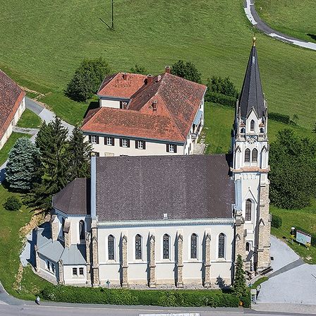 Eine Draufsicht auf eine Kirche mit Turmspitze, umgeben von einem grünen Feld, Häusern und einer Straße.