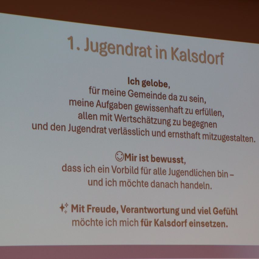Ein Präsentationsfolie mit fetter Schrift besagt '1. Jugendrat in Kalsdorf' und beschreibt weiter die Verpflichtung zu Gemeinschaftsaufgaben, die Ermutigung zu Respekt und Ernsthaftigkeit. Es wird erwähnt, ein Vorbild für Jugendliche zu sein und mit Freude, Verantwortung und Gefühl zu handeln.