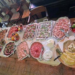 Ein langer Tisch ist mit verschiedenen Gerichten gefüllt, darunter Fleisch, Käse und Obst, mit ordentlich angeordneten Utensilien und Tellern.