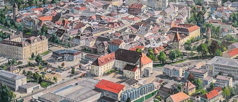Luftaufnahme einer Stadt mit vielen Gebäuden, Straßen und Bäumen. Mehrere Gebäude haben rote Dächer.