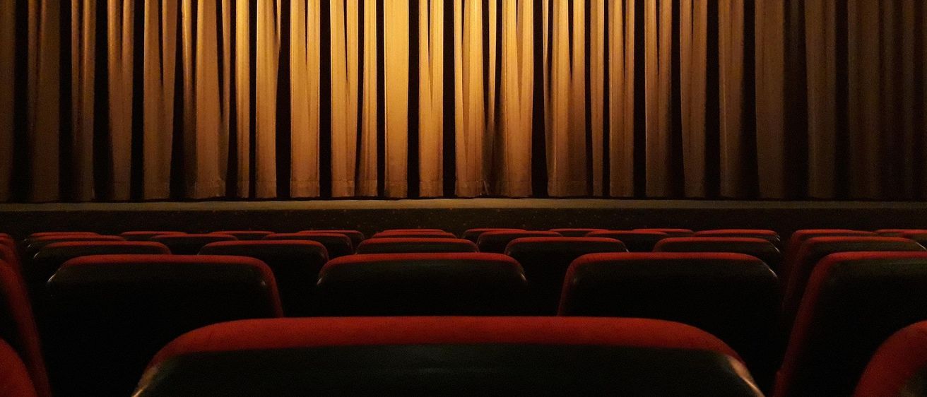 Ein leeres Theater mit Reihen roter Sitze und einem großen Vorhang, in warmem Licht getaucht.