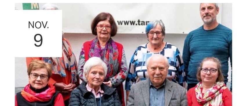 Eine Gruppe älterer Menschen posiert für ein Foto. Die Frau in der Mitte trägt ein Stethoskop. Der Mann rechts trägt einen grauen Mantel. Hinter ihnen ist ein weißer Banner mit dem Text www.tar.
