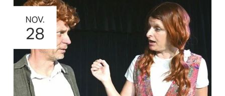 A man and a woman stand close together. The man is looking at the woman, who is speaking. The woman is wearing a floral vest. The man has a beard and is wearing a gray jacket. The background is black.