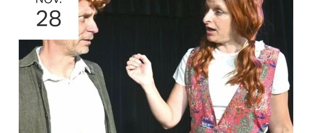 Ein Mann und eine Frau stehen sich gegenüber, die Frau spricht und zeigt mit dem Finger auf den Mann, der aufmerksam zuhört. Die Frau hat lange lockige rote Haare und trägt ein weißes ärmelloses Top mit Blumenmuster.