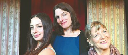 Drei Frauen lächeln und posieren für ein Foto. Eine in Blau, eine andere in Rot und die dritte trägt eine Schürze.