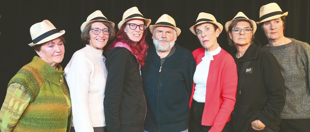 Eine Gruppe von sechs Personen posiert für ein Foto. Sie tragen alle Hüte und Brillen. Der Mann in der Mitte hat Bart und Schnurrbart. Hinter ihnen ist ein schwarzer Vorhang.