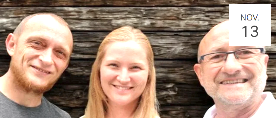 Drei Menschen lächeln für ein Foto, zwei Männer und eine Frau, stehen eng beieinander vor einer Holzwand.