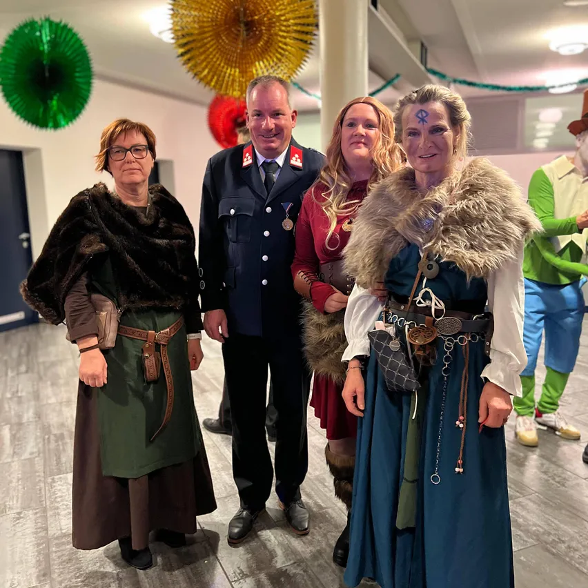 Eine Gruppe von Menschen in mittelalterlicher Kleidung, einer mit einem Pelzmantel, versammelt sich für ein Foto. Sie stehen auf einem Holzboden mit einem Mann in Uniform.